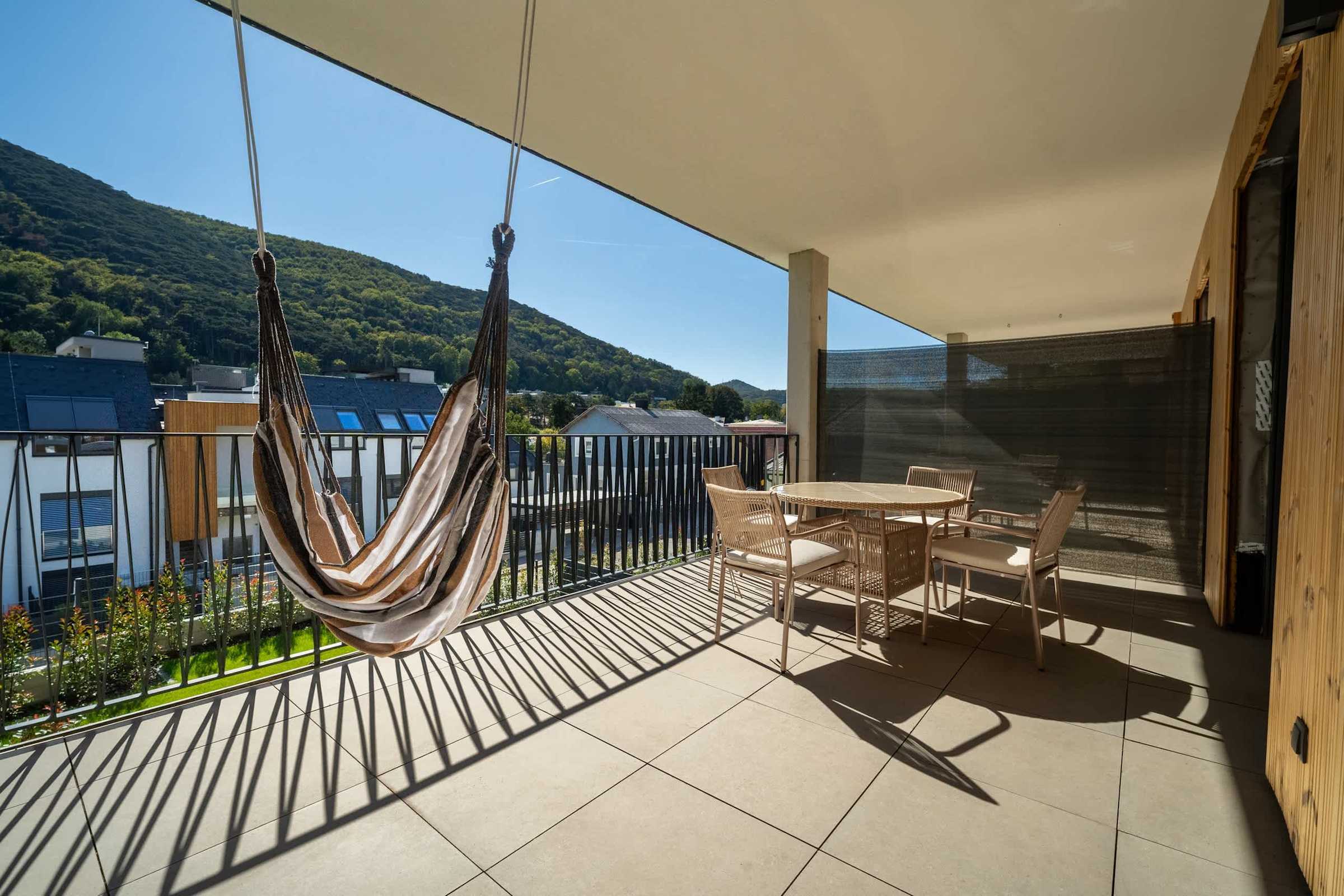 Covered balcony with hanging chair, dining table and views of the wooded hills